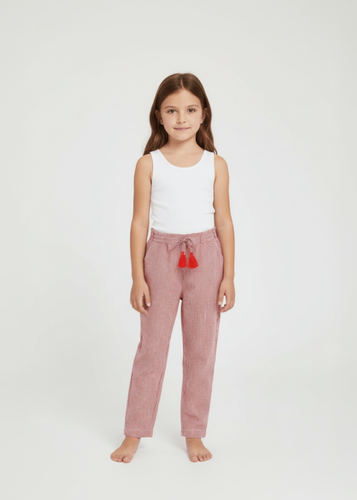 Young girl wearing a white top and pink pants with red pom-poms on a white background